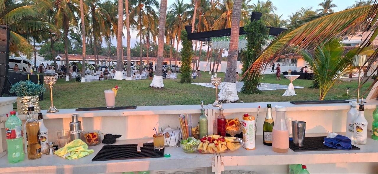Barra de cócteles montada en un jardín junto a palmeras durante una boda