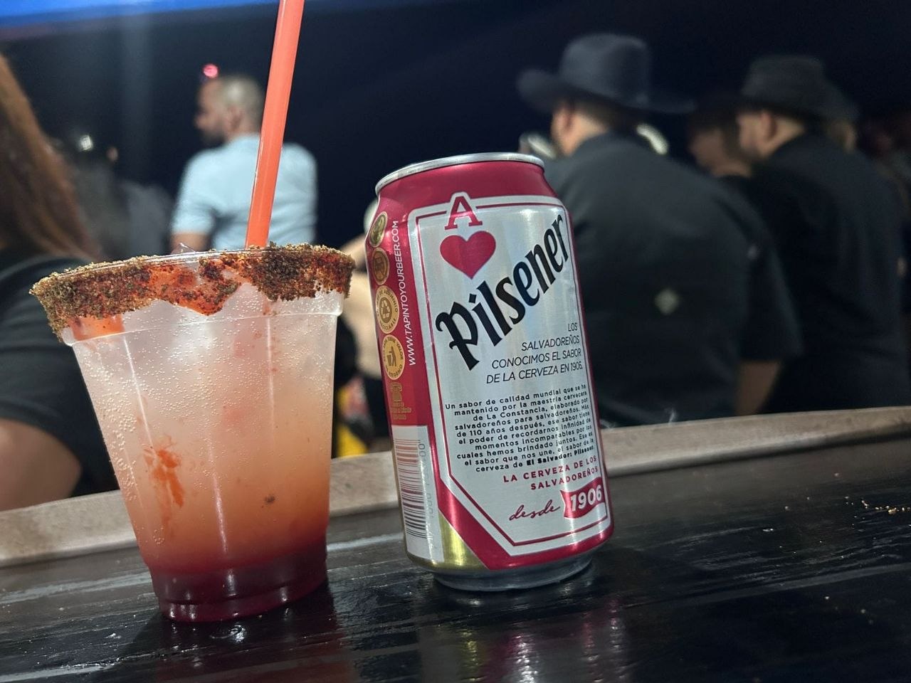 Cóctel con borde escarchado junto a una cerveza Pilsener en un evento nocturno
